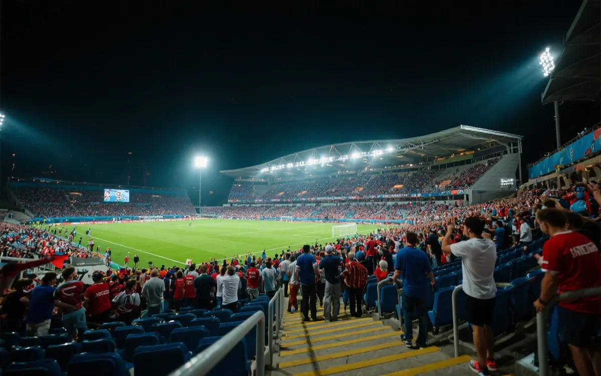 夜晚灯光下的现代足球场外景，球迷涌入看台